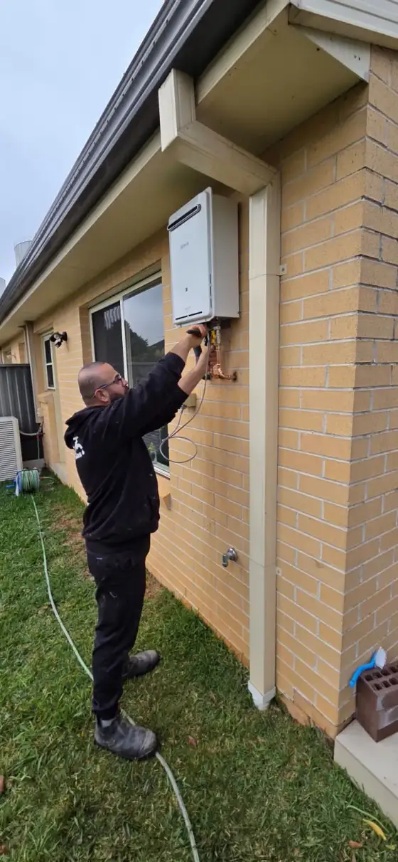 Antons plumber inspecting pipe connections on an outdoor hot water system