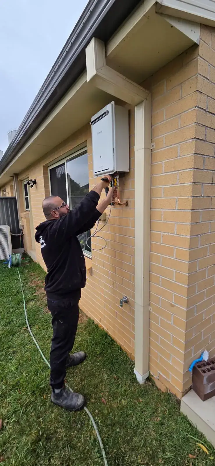 Antons plumber inspecting pipe connections on an outdoor hot water system